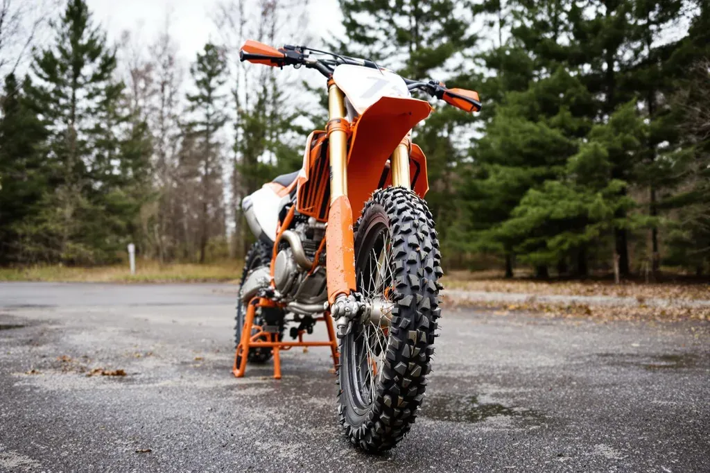 Enduro-Motorrad mit groben Stollenreifen steht auf einem nassen Waldparkplatz, aus der Froschperspektive fotografiert