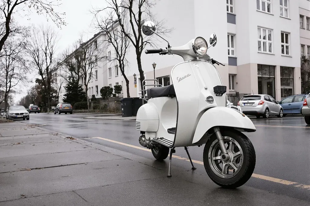 Weißer Motorroller steht auf dem Seitenständer am Rand einer nassen Wohnstraße