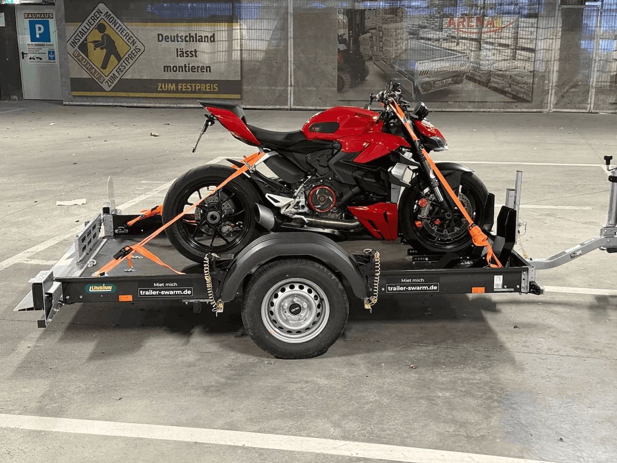 Hochgekippter Unsinn-Anhänger mit verzurrter Ducati Streetfighter, fahrbereit abgestellt in der Tiefgarage