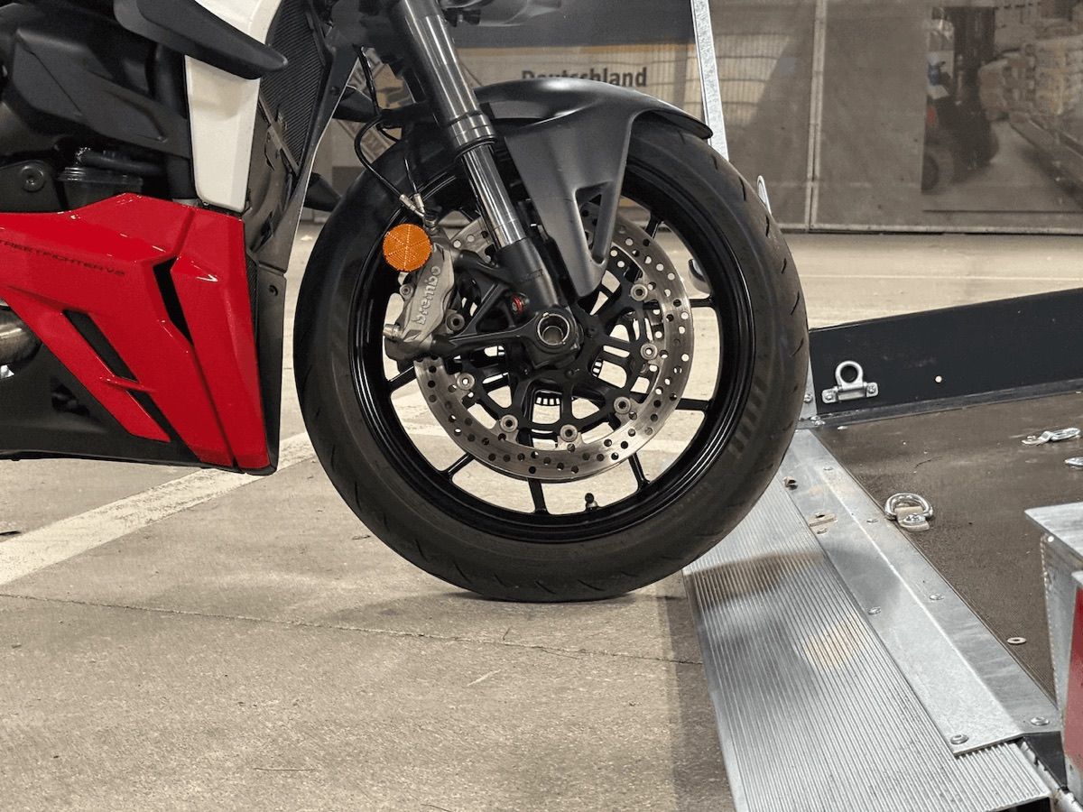 Vorderrad einer roten Ducati Streetfighter am verzinkten Auffahrkeil der abgekippten Ladefläche